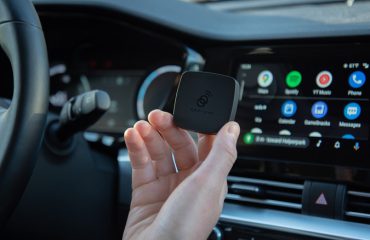 AAWireless Android Auto adapter held in front of dashboard and android auto screen